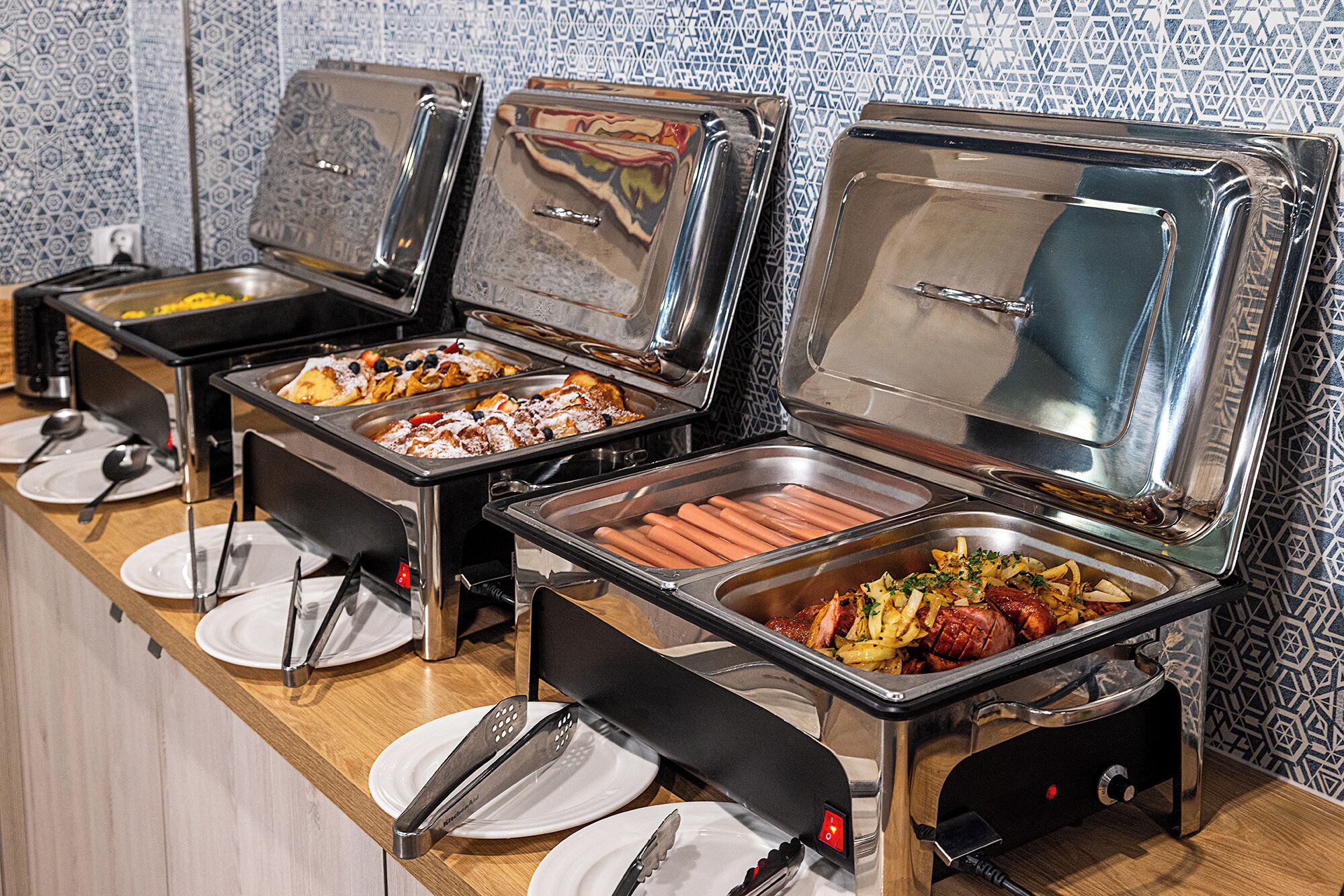 A buffet with various food items, including hot dogs and a dish with meat and vegetables.