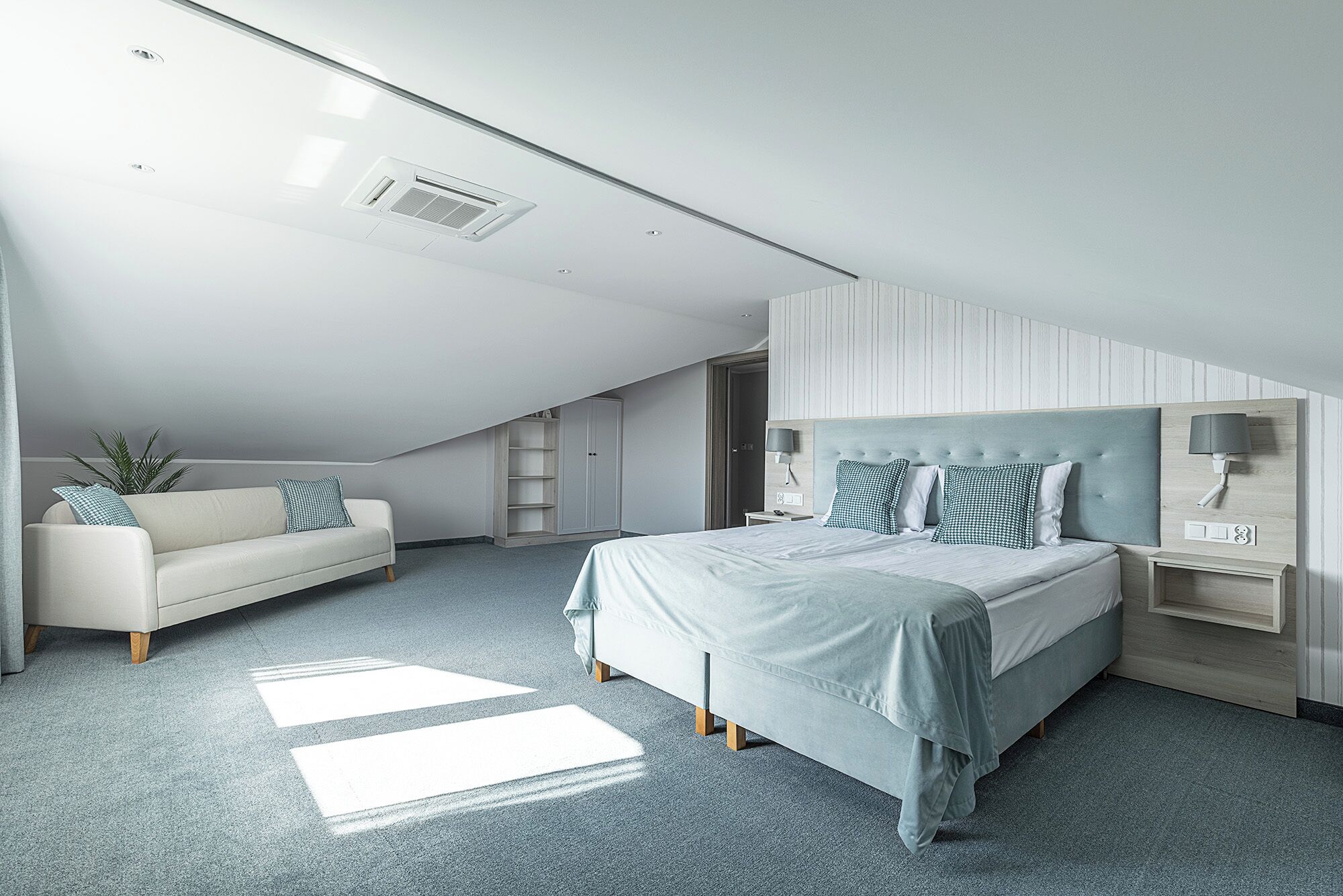 A modern bedroom with a bed, a sofa, a nightstand, and a wall-mounted lamp.