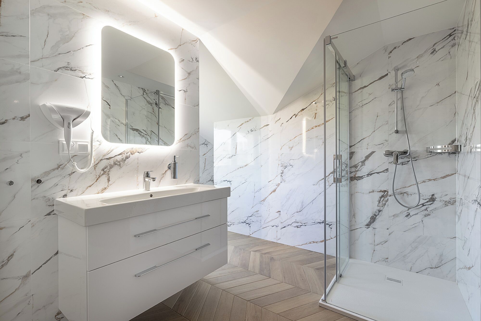 Une salle de bain moderne avec un meuble-lavabo en marbre, une cabine de douche en verre et un sol à motifs en chevrons.