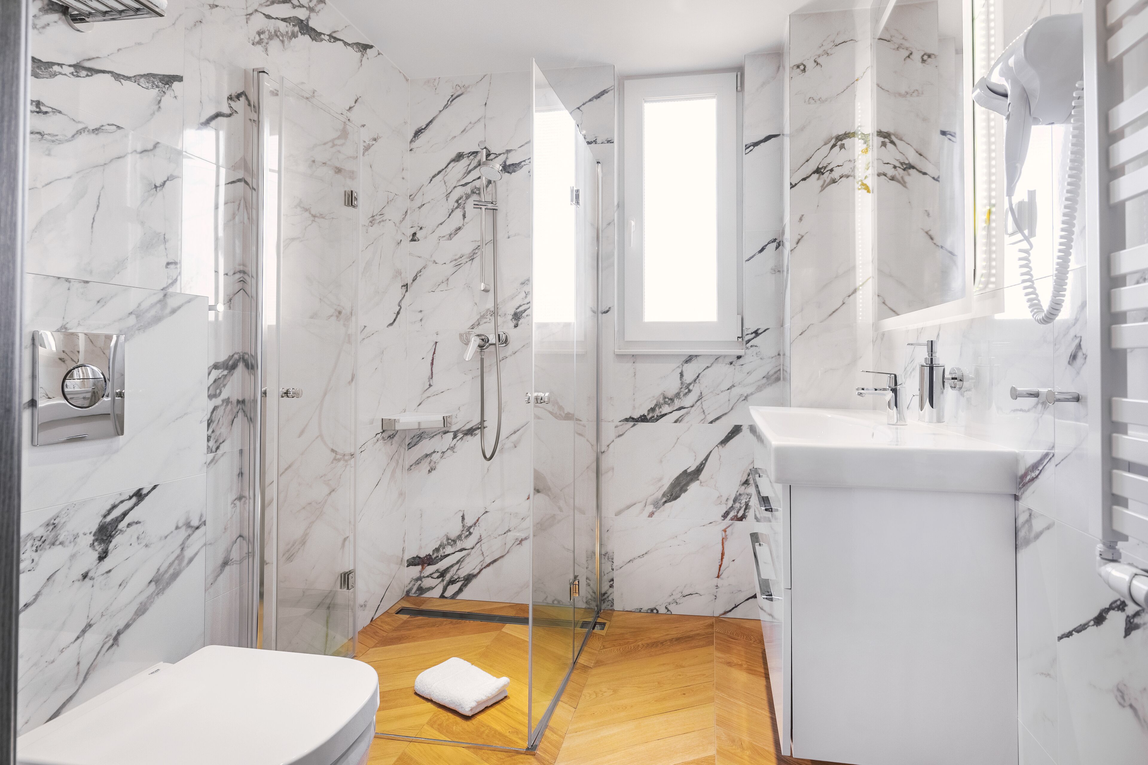 A modern bathroom with a glass-enclosed shower, a wooden floor, and a white sink.