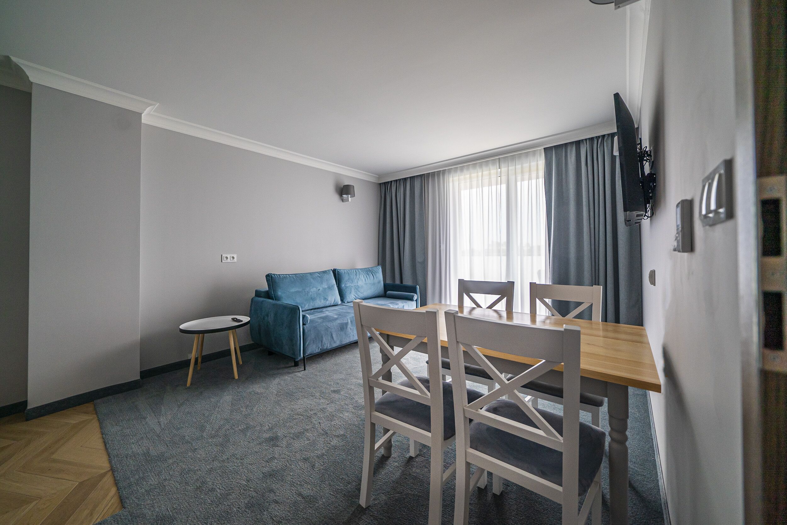 A modern living room with a blue sofa, a small round table, and a wooden dining table with chairs.