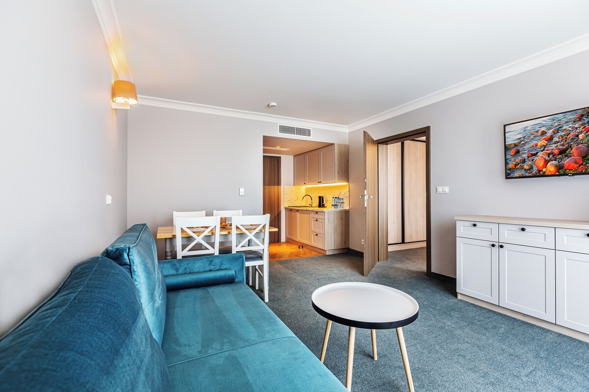 A modern living room with a blue sofa, a small round table, and a kitchen in the background.