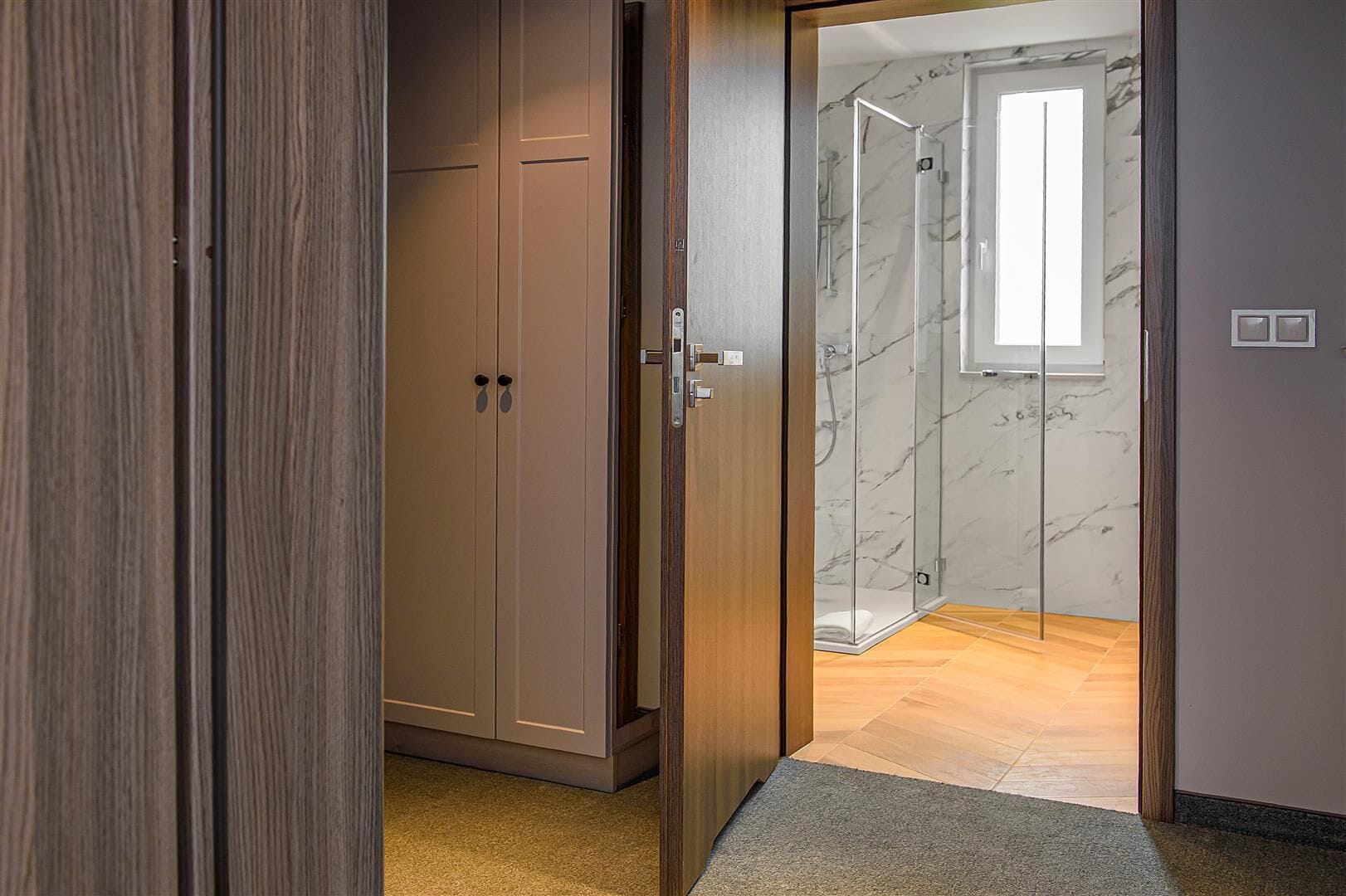 A room with a wooden wardrobe, a glass shower enclosure, and a marble wall.