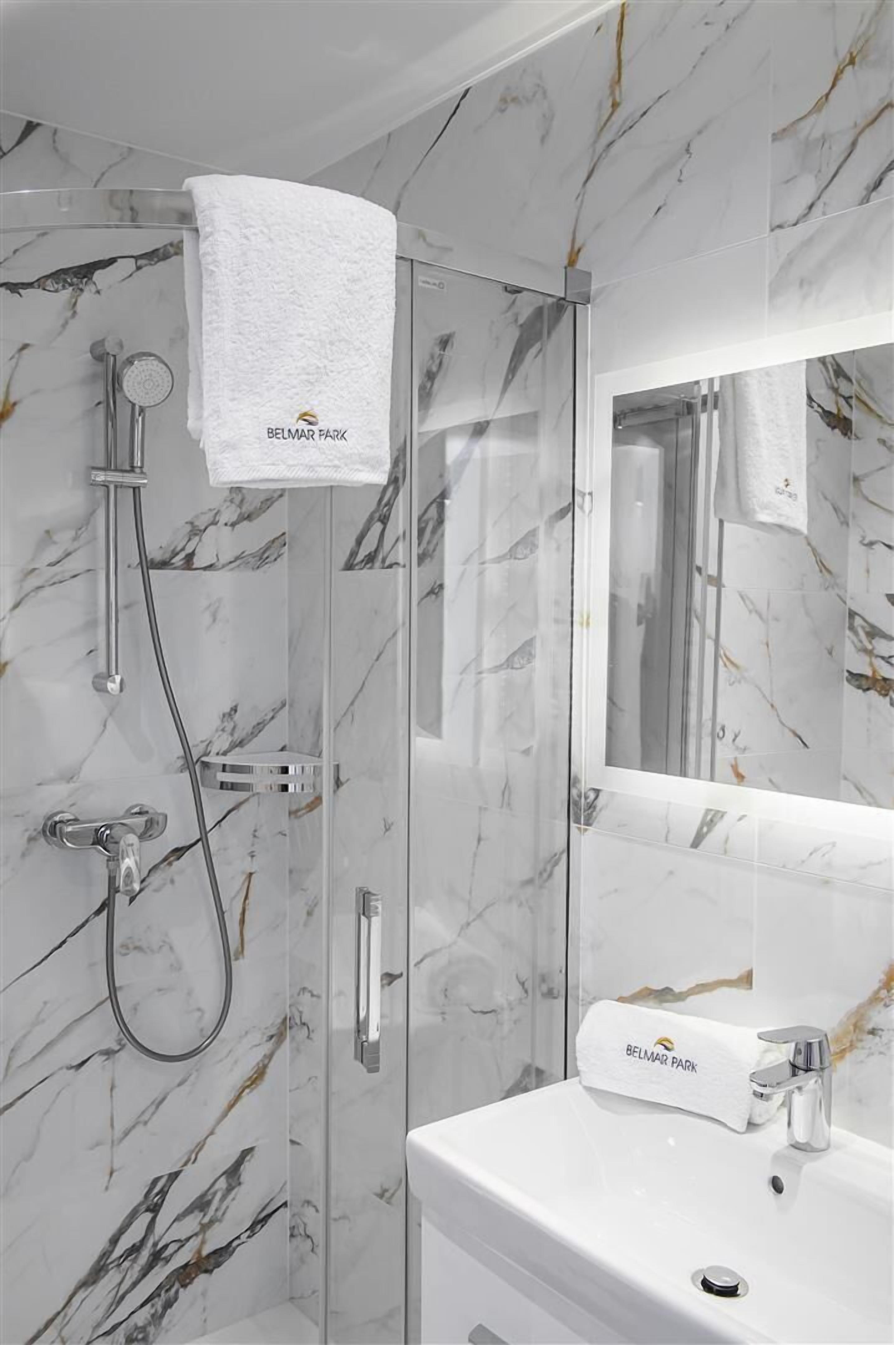 Un baño con ducha acristalada, un lavabo blanco y una pared con diseño de mármol.