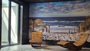 A spa area with a hot tub, two wooden lounge chairs, and a beach mural on the wall. - Belmar Park (Wladyslawowo)