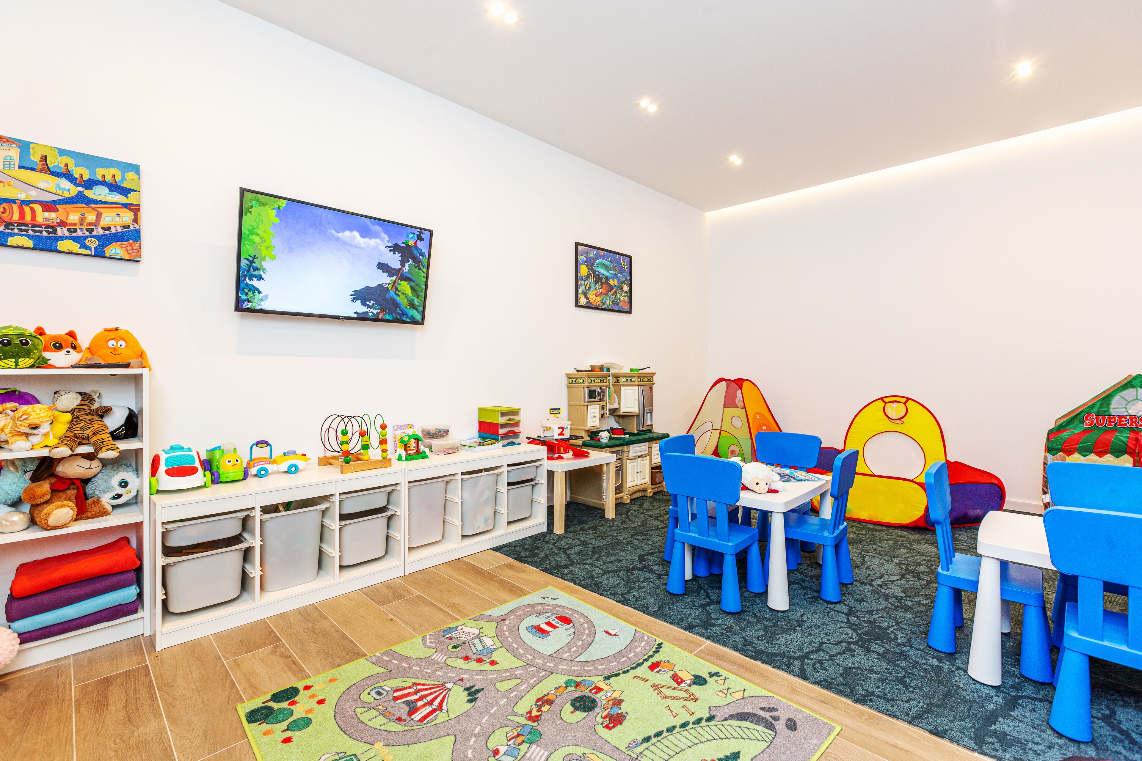 A children's playroom with colorful toys, a play table, and a carpet with a road scene.