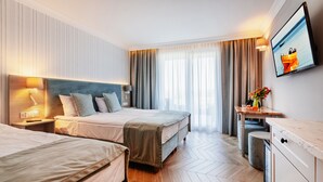 A hotel room with two beds, a desk, a chair, a TV, and a large window with curtains. - Belmar Park (Wladyslawowo)