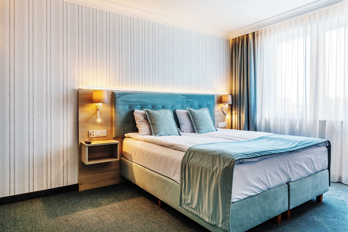 A hotel room with a bed, bedside tables, and a view of the outdoors.