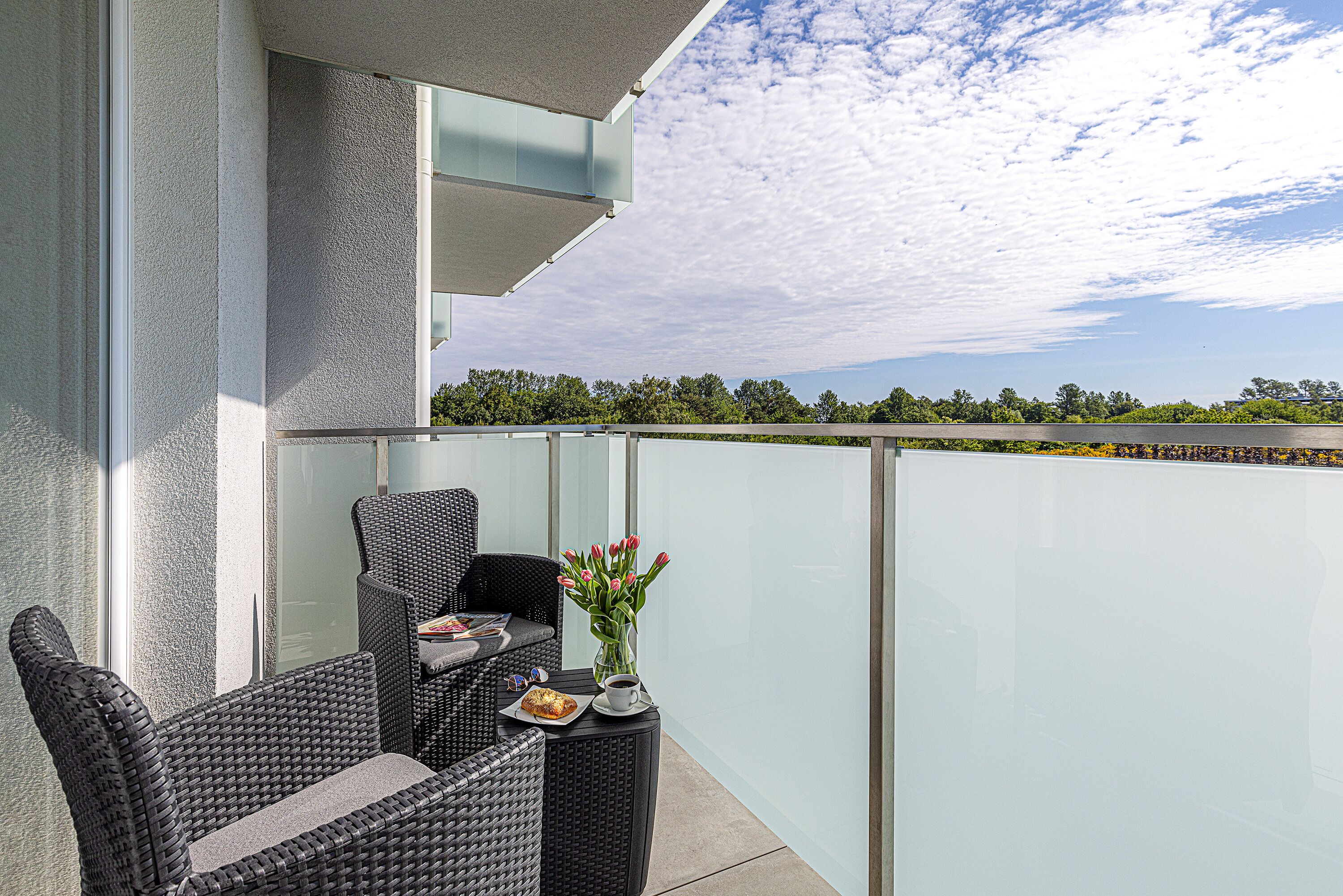 A balcony with wicker furniture, a vase with flowers, and a table with a plate and a cup.