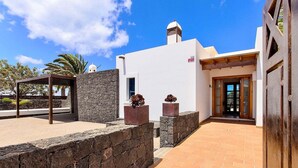 A modern building with a white exterior, a stone wall, and a wooden pergola. - Villa in Marina Rubicon with Pool (Playa Blanca)