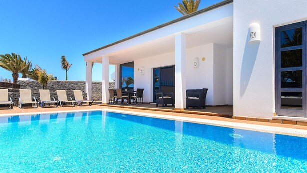 A modern pool area with lounge chairs and a covered seating area. - Villa in Marina Rubicon with Pool (Playa Blanca)
