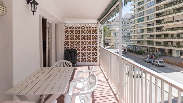 A balcony with a white table and chairs, a decorative wall, and a view of a multi-story building and street. - SAINT GERMAIN, A-2º-4 (Cullera)