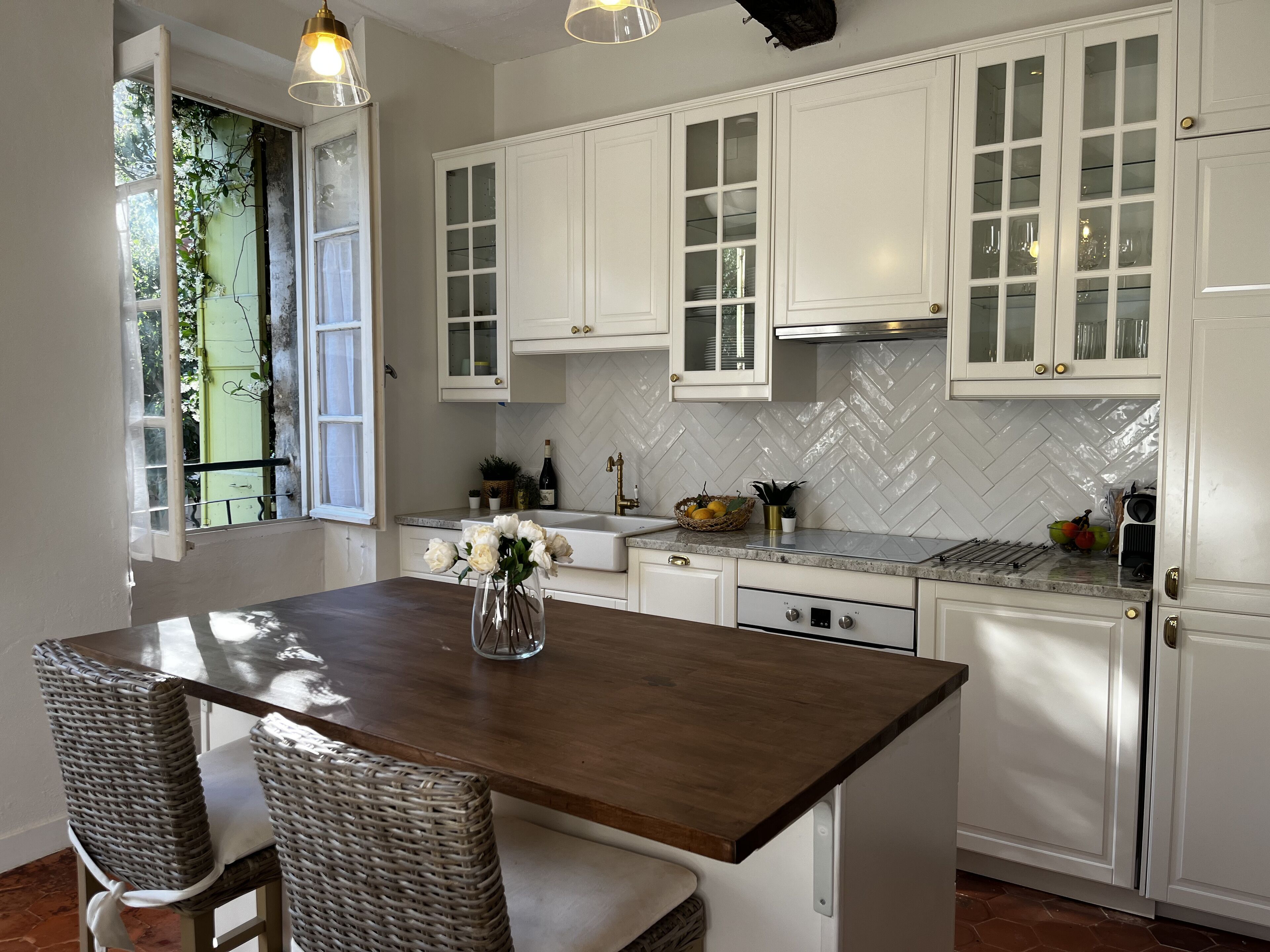 A kitchen with white cabinets, a herringbone tile backsplash, and a wooden island with chairs.