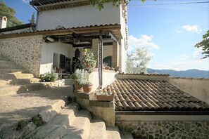 Un bâtiment traditionnel en pierre, avec un toit en tuiles, un escalier en pierre et des plantes en pot.