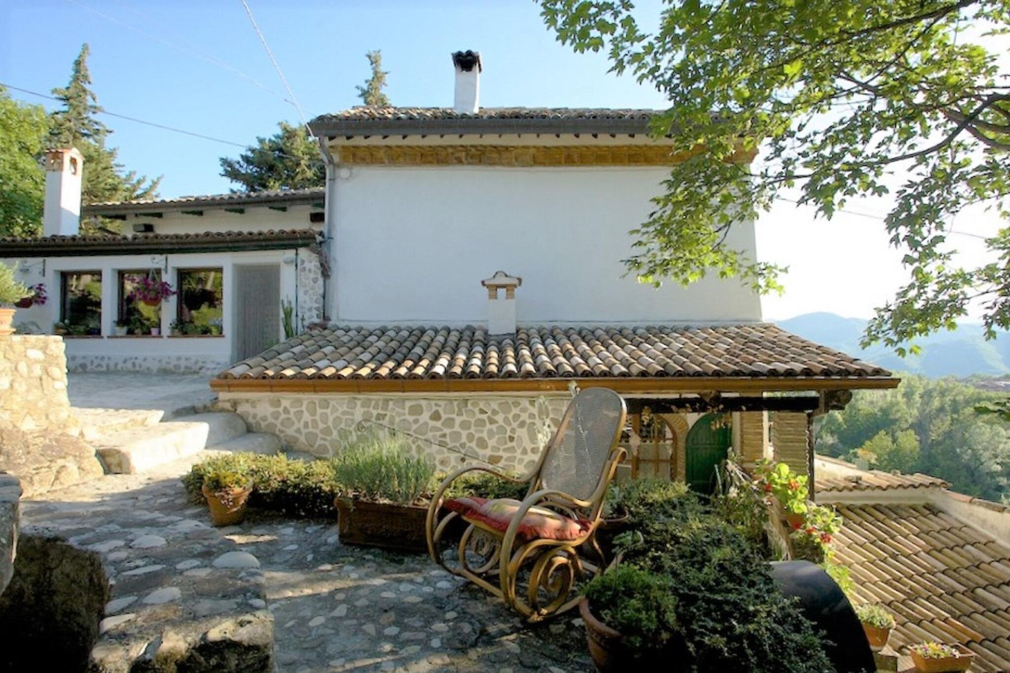 Un bâtiment rustique en pierre, avec un toit en tuiles, un petit porche et une chaise.