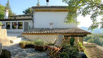 Un bâtiment rustique en pierre, avec un toit en tuiles, un petit porche et une chaise.