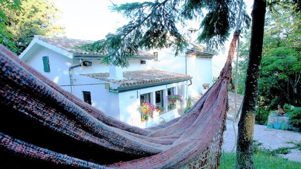 A hammock in a lush garden with a white building in the background.