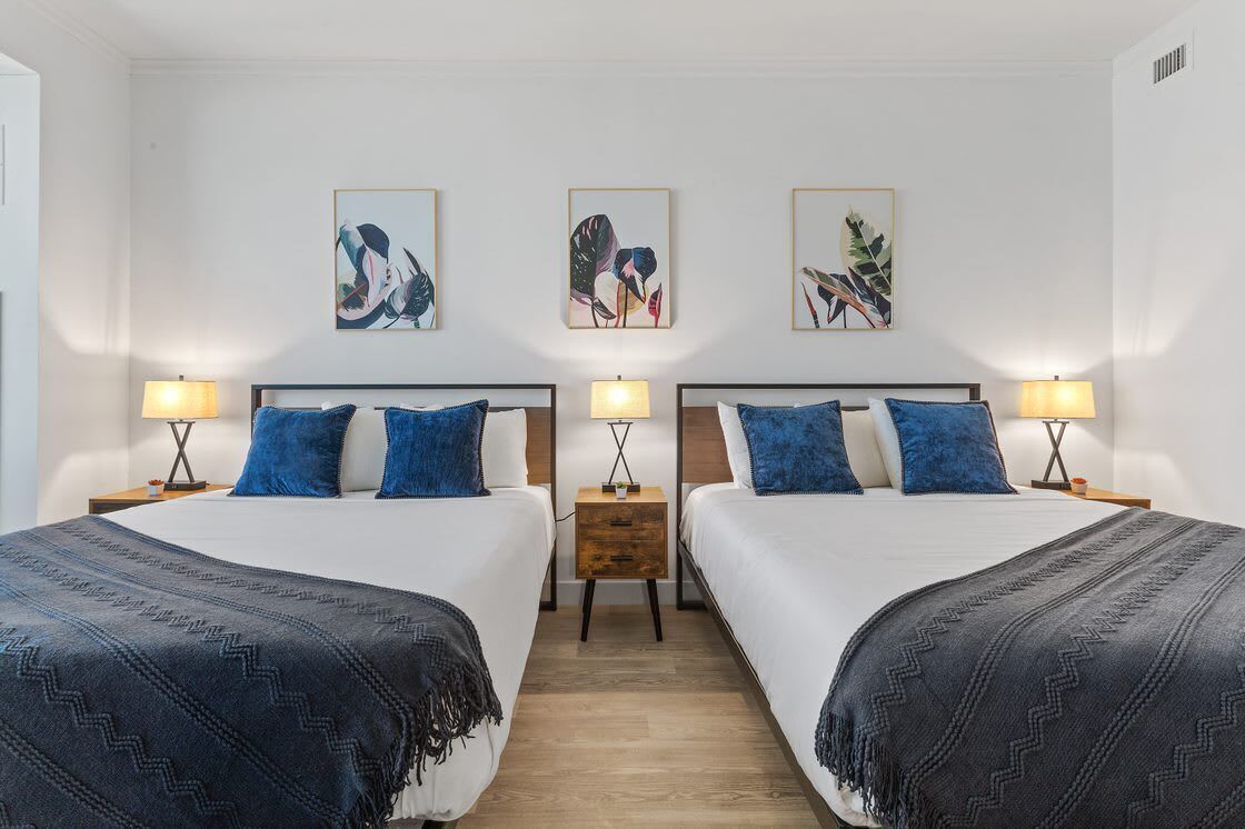 Una habitación doble con dos camas, cada una con una mesita de noche y una lámpara. Hay tres cuadros enmarcados en la pared sobre las camas.