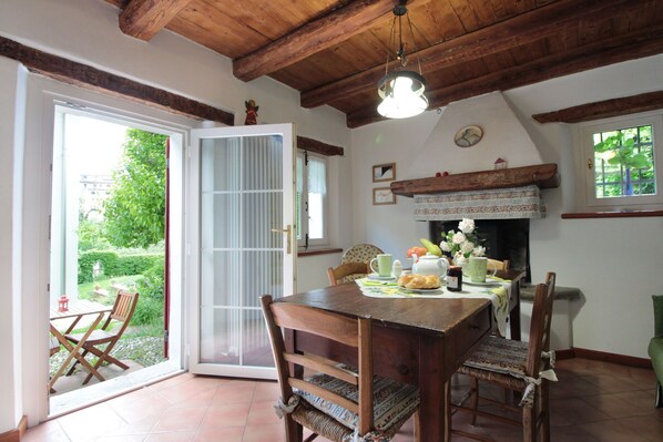 A dining area with a wooden table and chairs, a fireplace, and a view of a garden through an open door.
