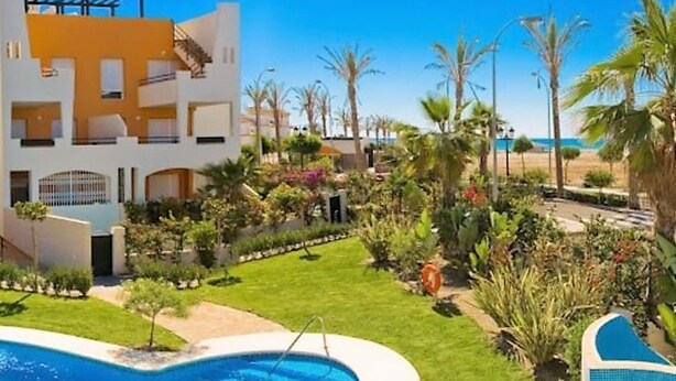 A hotel with a pool, a well-maintained garden, and a view of the beach.