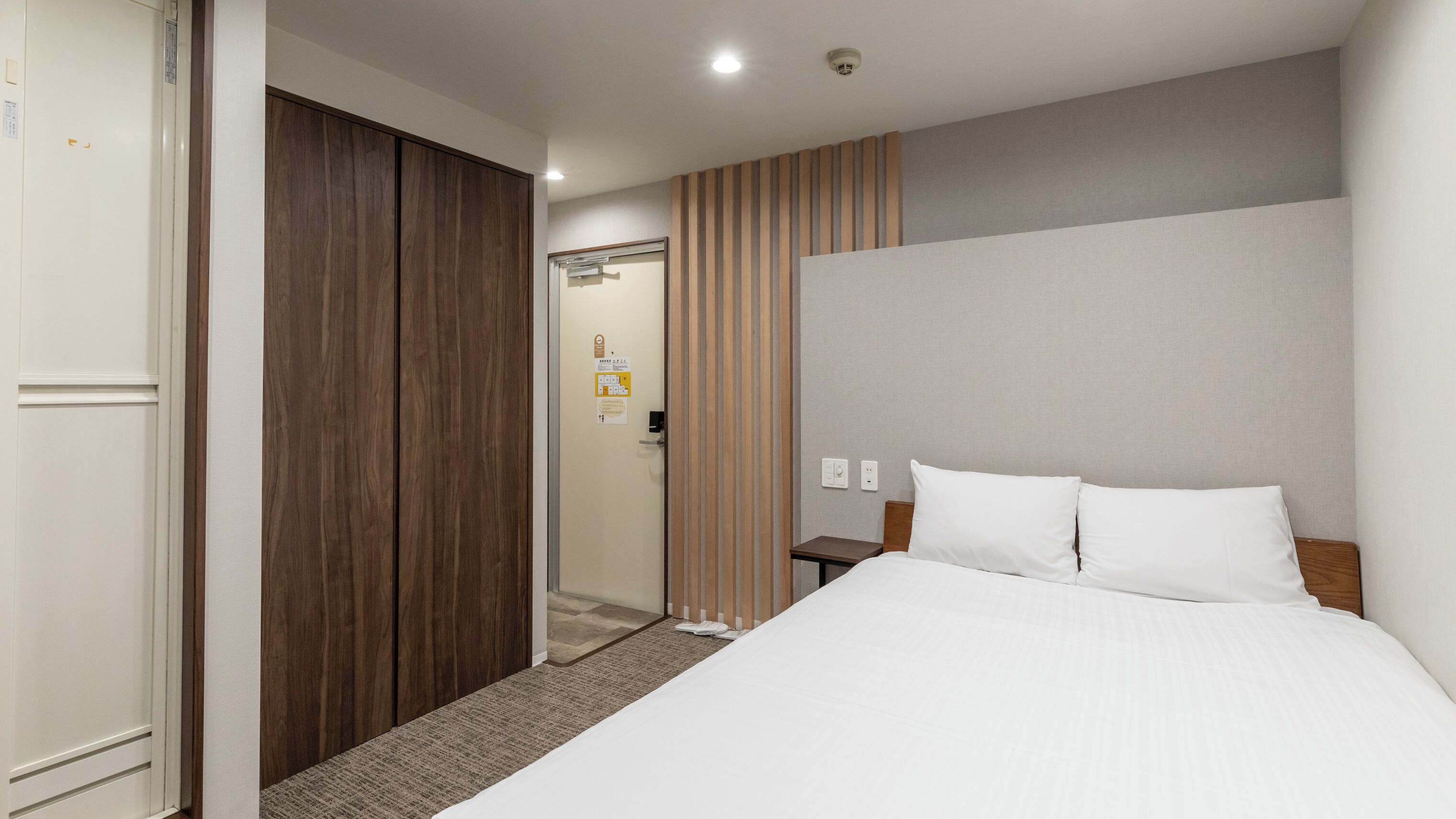 A hotel room with a bed, a wooden wardrobe, a door, and a wall with a striped pattern.