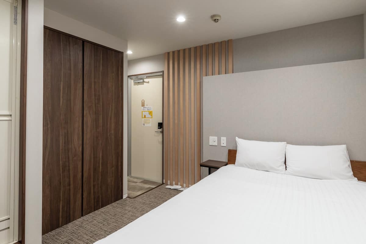 A hotel room with a bed, a wooden wardrobe, a door, and a wall with a striped pattern.