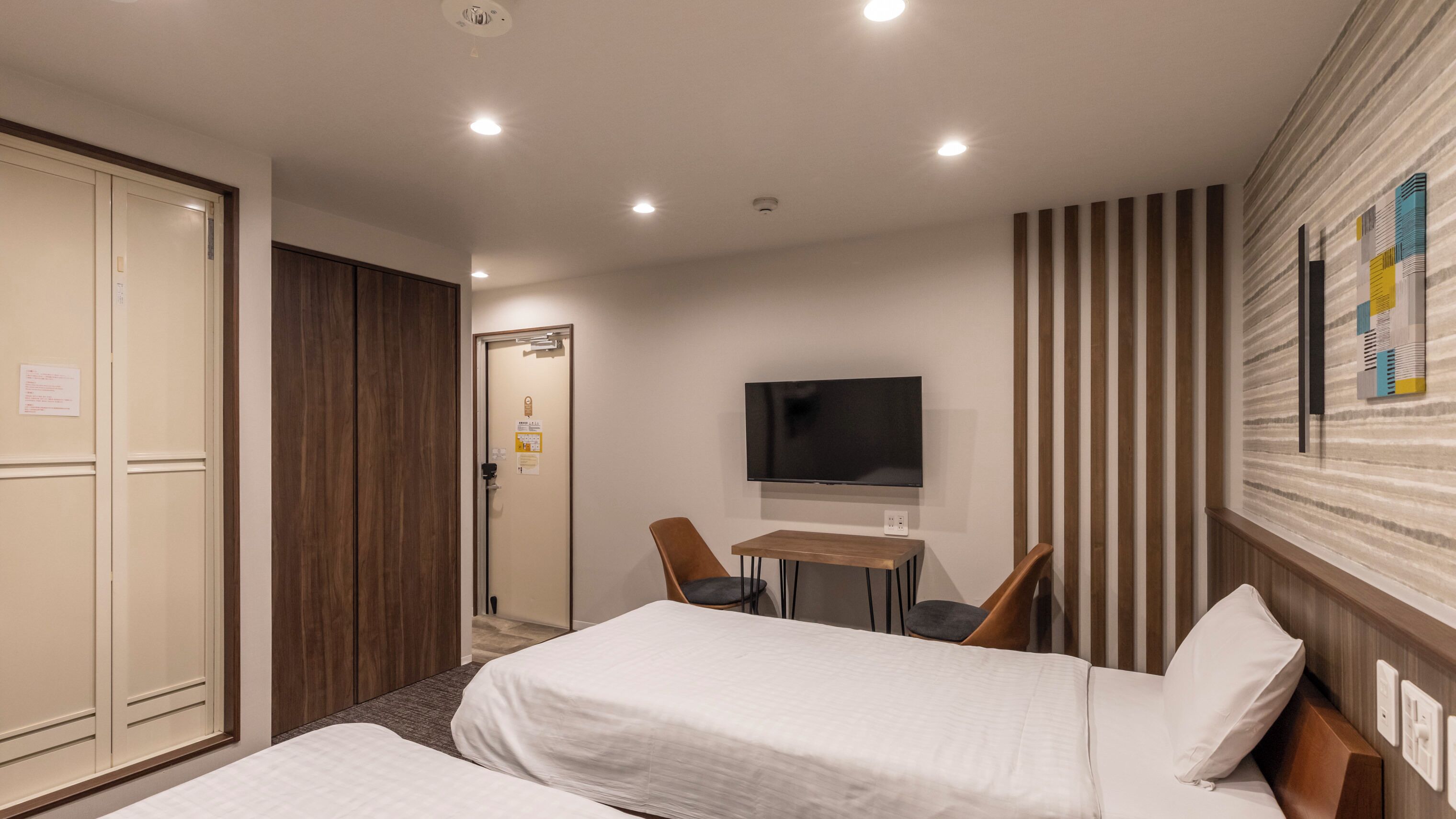A hotel room with two beds, a TV, a desk, and a striped wall.
