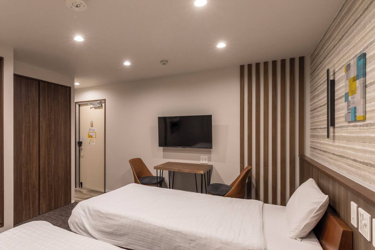 A hotel room with two beds, a TV, a desk, and a striped wall.