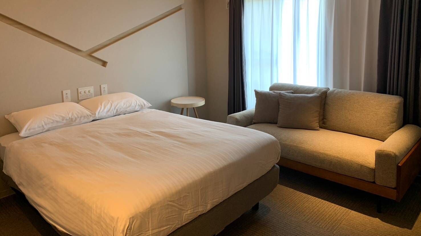 A hotel room with a bed, a sofa, a small round table, and a window with curtains.