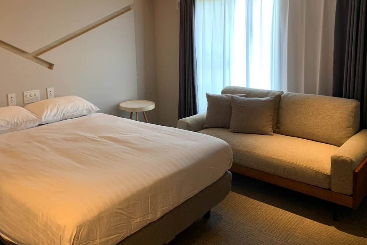 A hotel room with a bed, a sofa, a small round table, and a window with curtains.