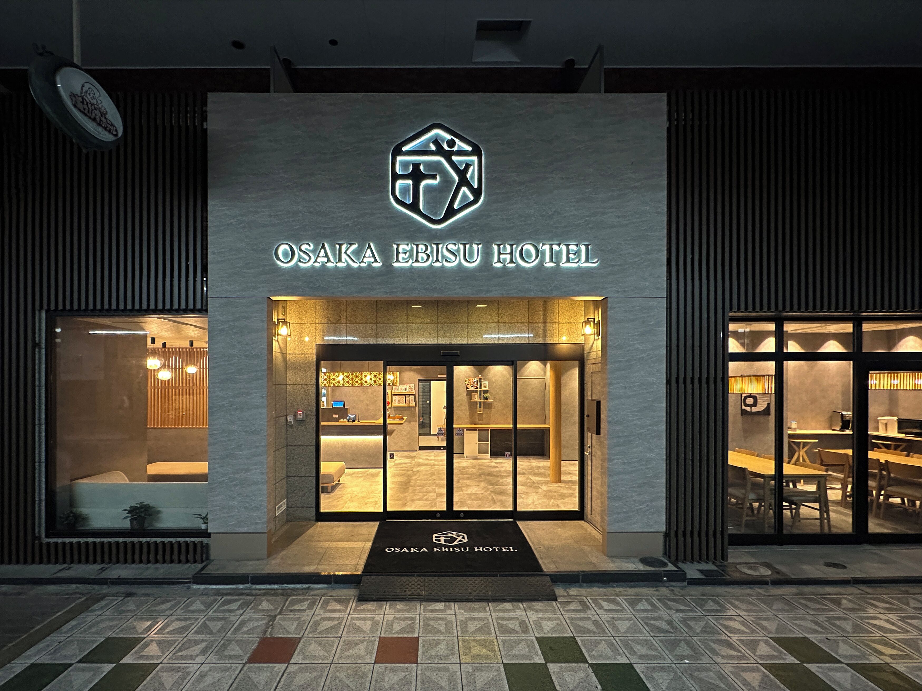 The exterior of Osaka Ebisu Hotel with a modern design, a reception area, and a visible dining space.