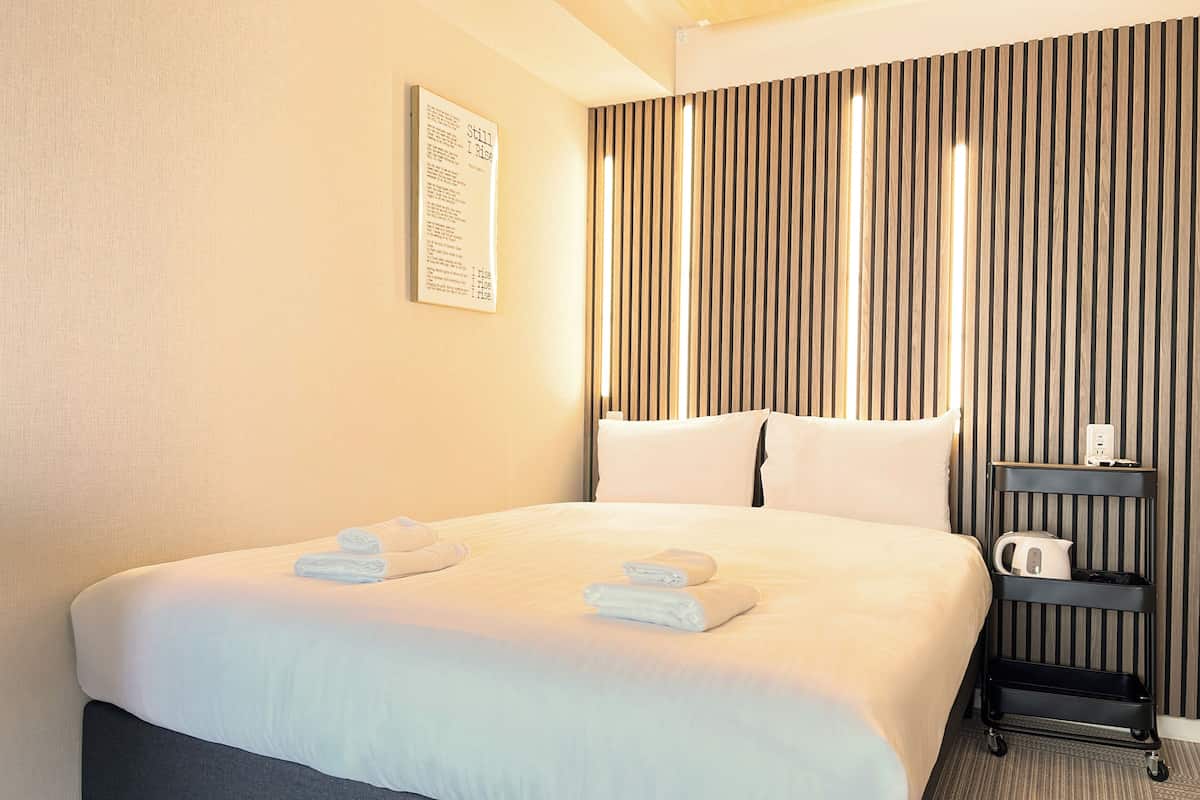 A hotel room with a large bed, a bedside table with a kettle, and a wall-mounted sign.