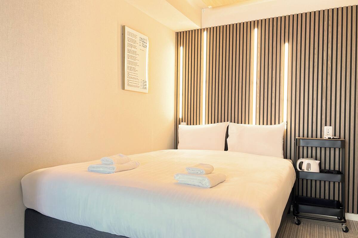 A hotel room with a large bed, a bedside table with a kettle, and a wall-mounted sign.