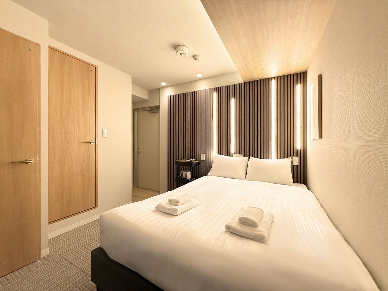 A hotel room with a large bed, wooden wardrobe, and a modern wall panel design.