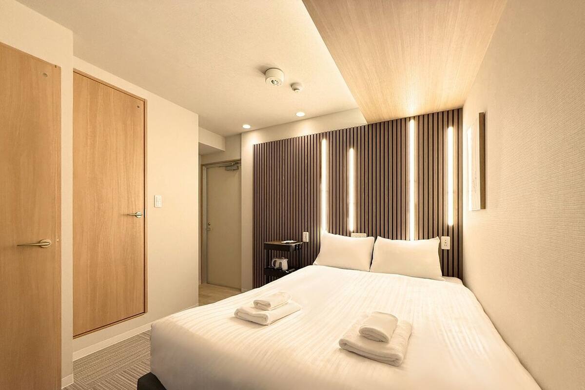 A hotel room with a large bed, wooden wardrobe, and a modern wall panel design.