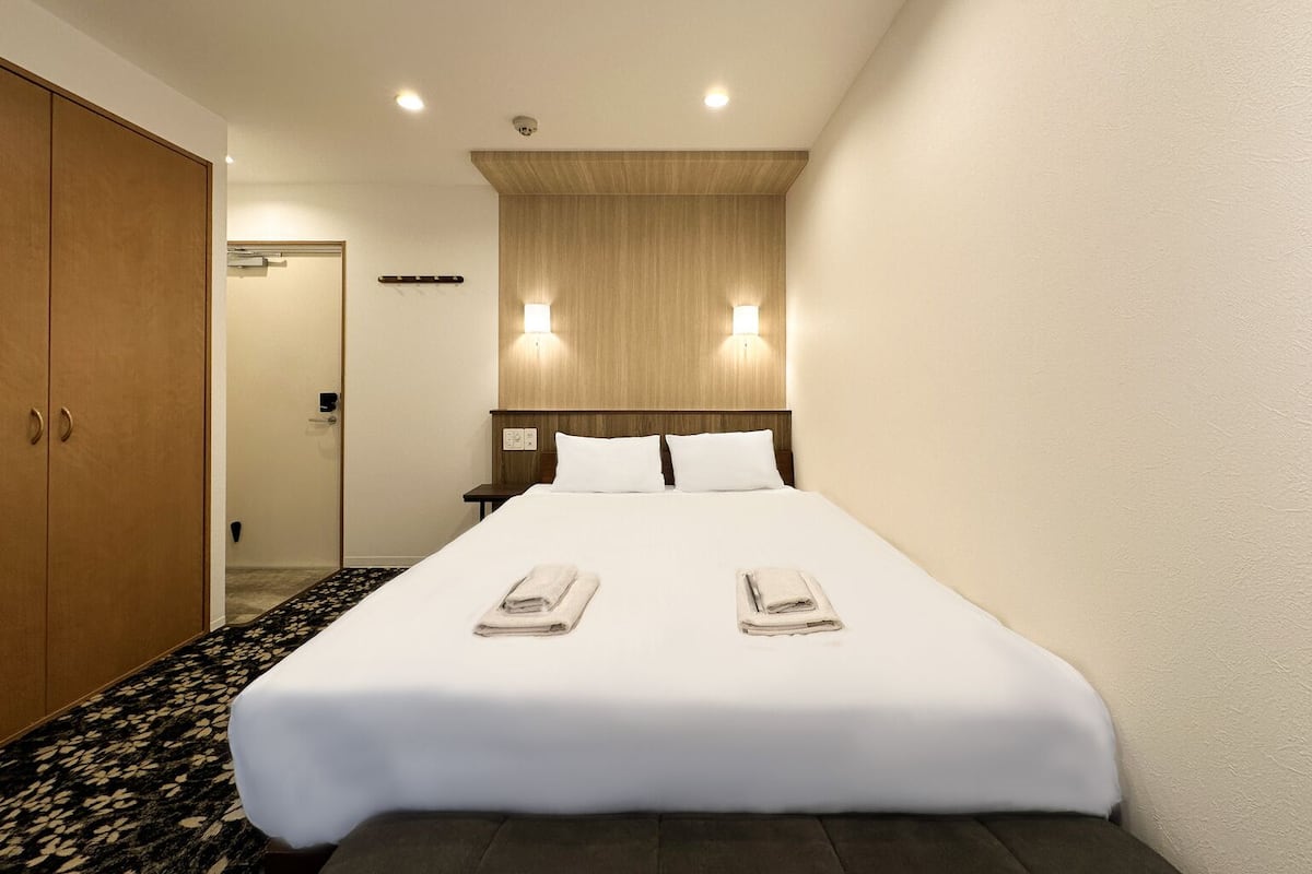 A hotel room with a bed, two bedside lamps, a wooden headboard, and a carpeted floor.