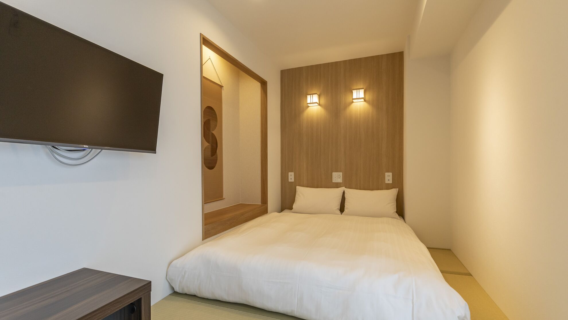 A modern hotel room with a large bed, a flat-screen TV mounted on the wall, and two wall-mounted lights.