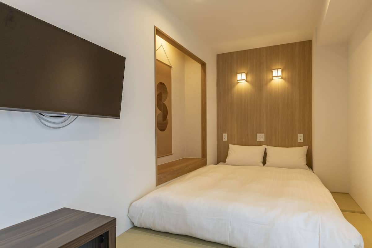 A modern hotel room with a large bed, a flat-screen TV mounted on the wall, and two wall-mounted lights.