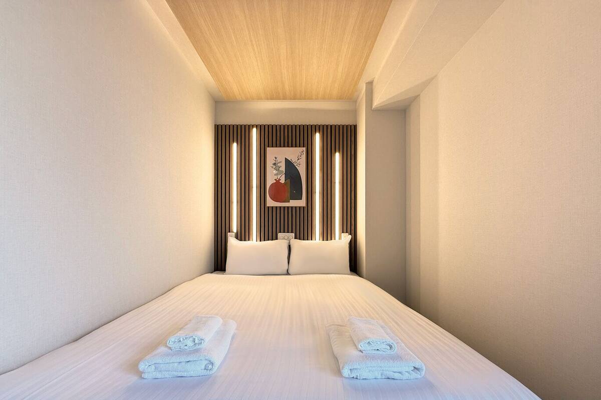 A modern hotel room with a large bed, two pillows, a headboard with vertical slats, and a framed artwork on the wall.