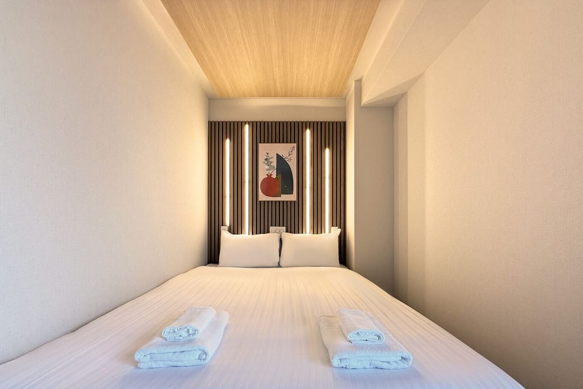 A modern hotel room with a large bed, two pillows, a headboard with vertical slats, and a framed artwork on the wall.