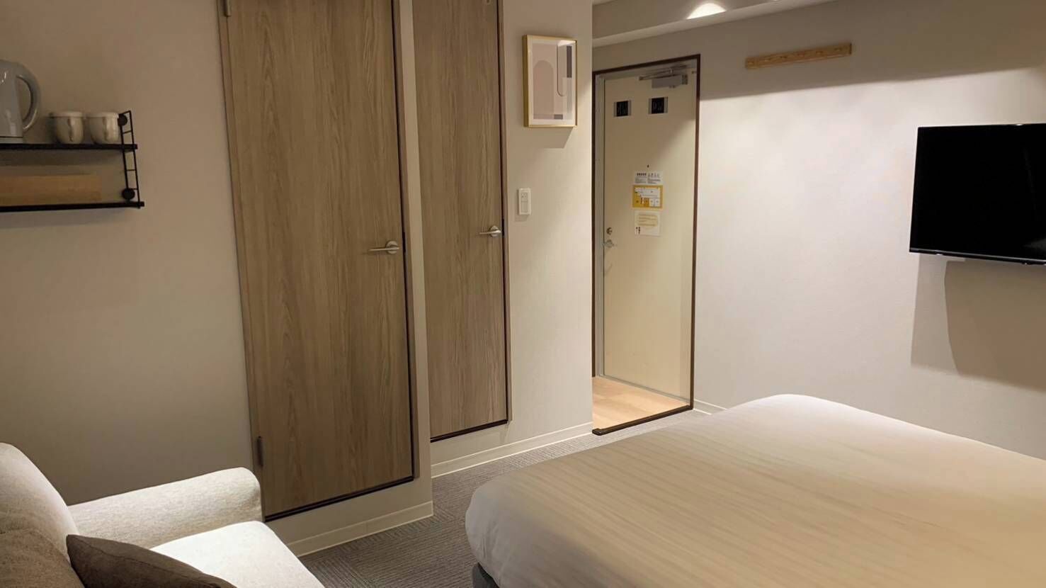 A hotel room with a bed, a wardrobe, a television, and a shelf with cups.