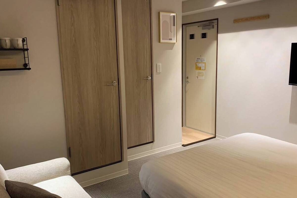 A hotel room with a bed, a wardrobe, a television, and a shelf with cups.