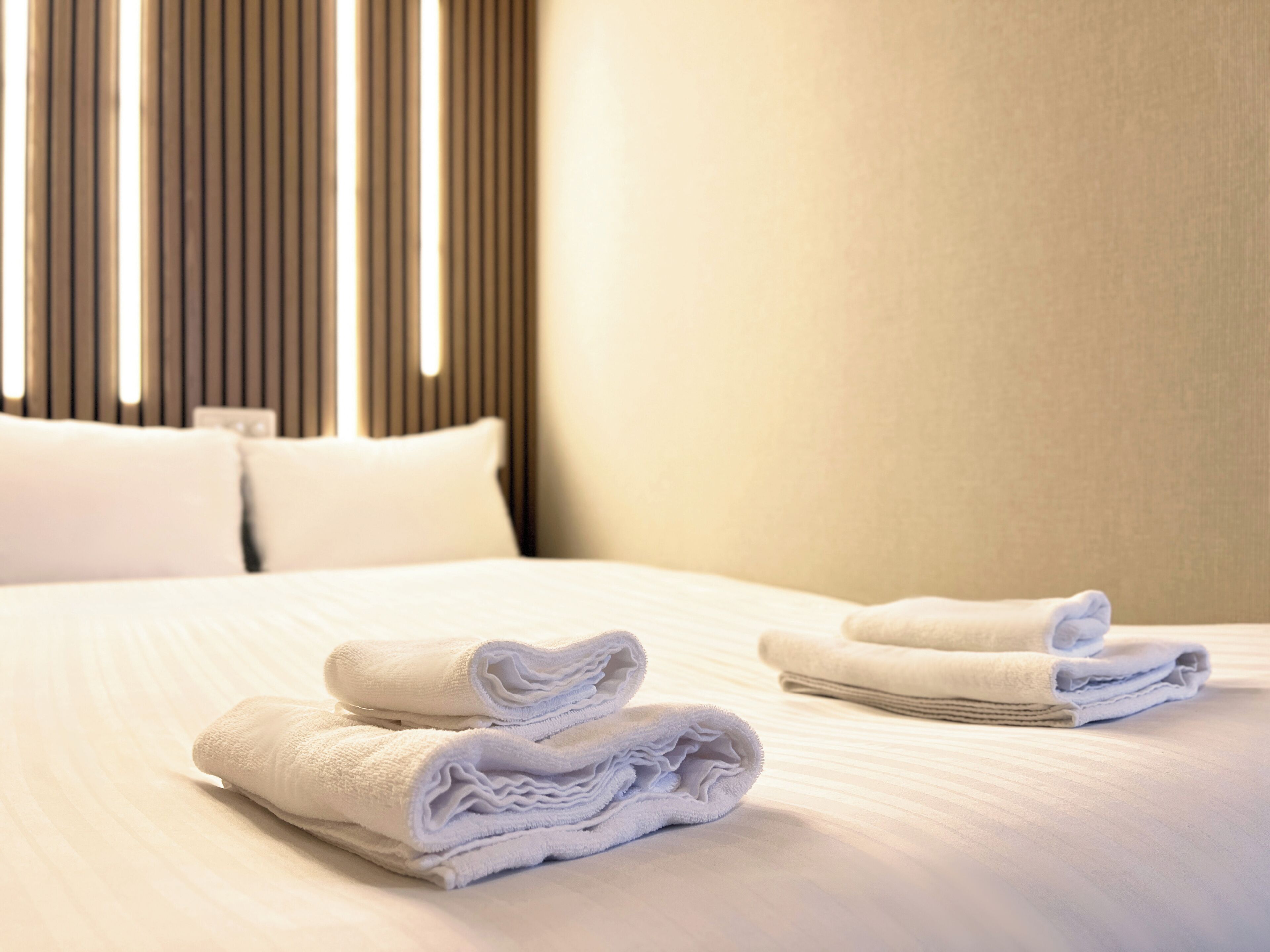 A neatly made bed with folded white towels and a headboard with vertical slats.
