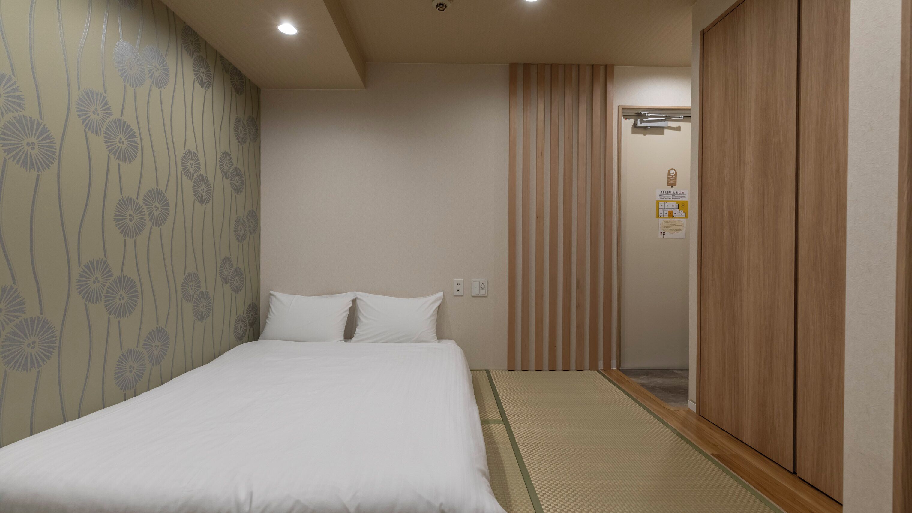 A hotel room with a bed, a wooden wardrobe, a wall with a floral pattern, and a sliding door.