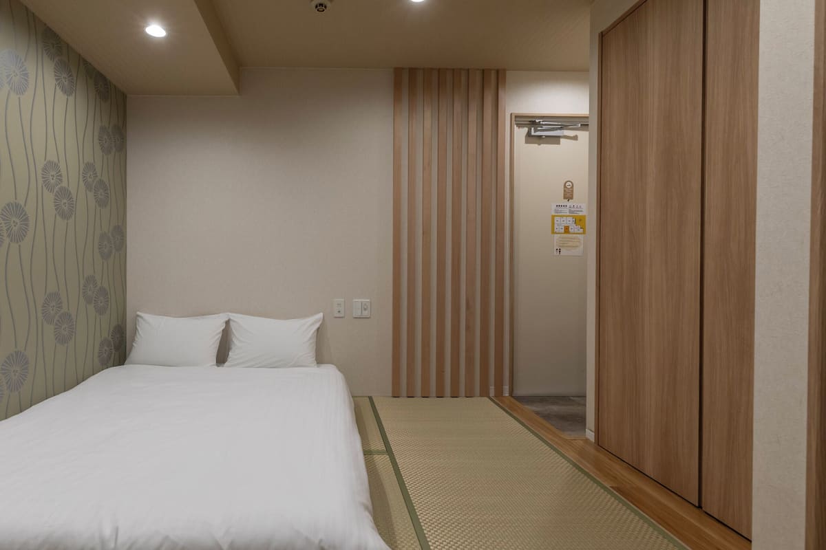 A hotel room with a bed, a wooden wardrobe, a wall with a floral pattern, and a sliding door.