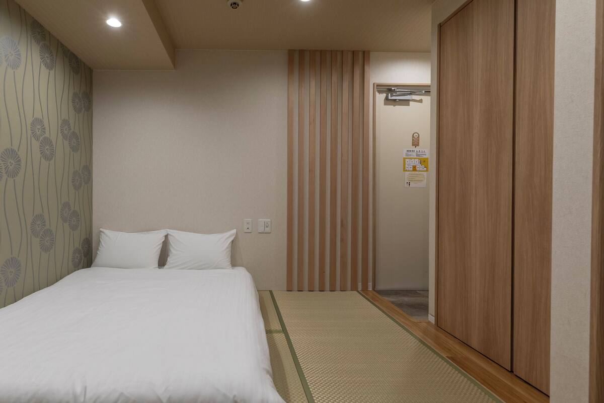 A hotel room with a bed, a wooden wardrobe, a wall with a floral pattern, and a sliding door.