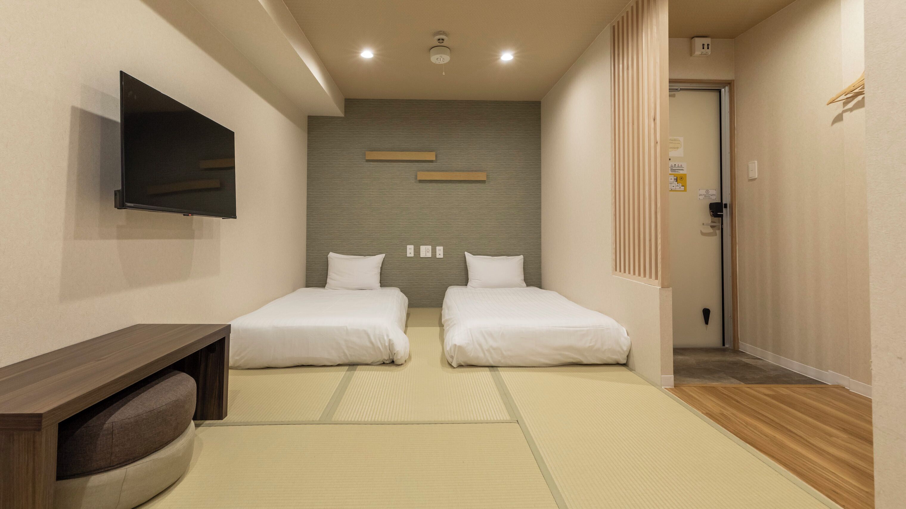 A hotel room with two beds, a TV, a wooden desk, and a tatami mat floor.