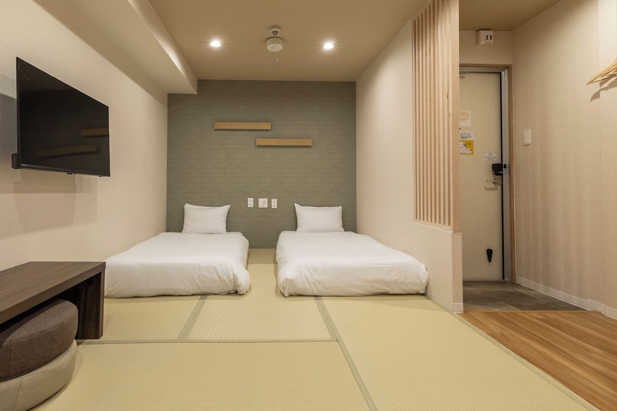A hotel room with two beds, a TV, a wooden desk, and a tatami mat floor.