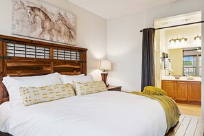 A bedroom with a wooden headboard, a large bed with white bedding and yellow pillows, a bedside lamp, a mirror, and a bathroom with a vanity and sink. - Beautifully Furnished Home in Power Ranch ~ Steps away from Community Pool & Spa (Gilbert)