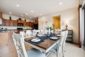 A modern kitchen with wooden cabinets, a central island, and a dining area with a wooden table set for four. - Beautifully Furnished Home in Power Ranch ~ Steps away from Community Pool & Spa (Gilbert)